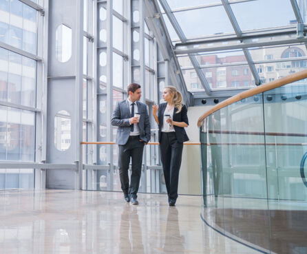 Businessman and businesswoman walk together and talk about business holding coffee in hand