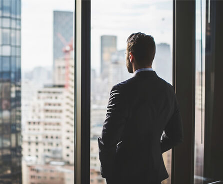 Business man in suit in office looking at modern city with skyscrapers through panoramic window